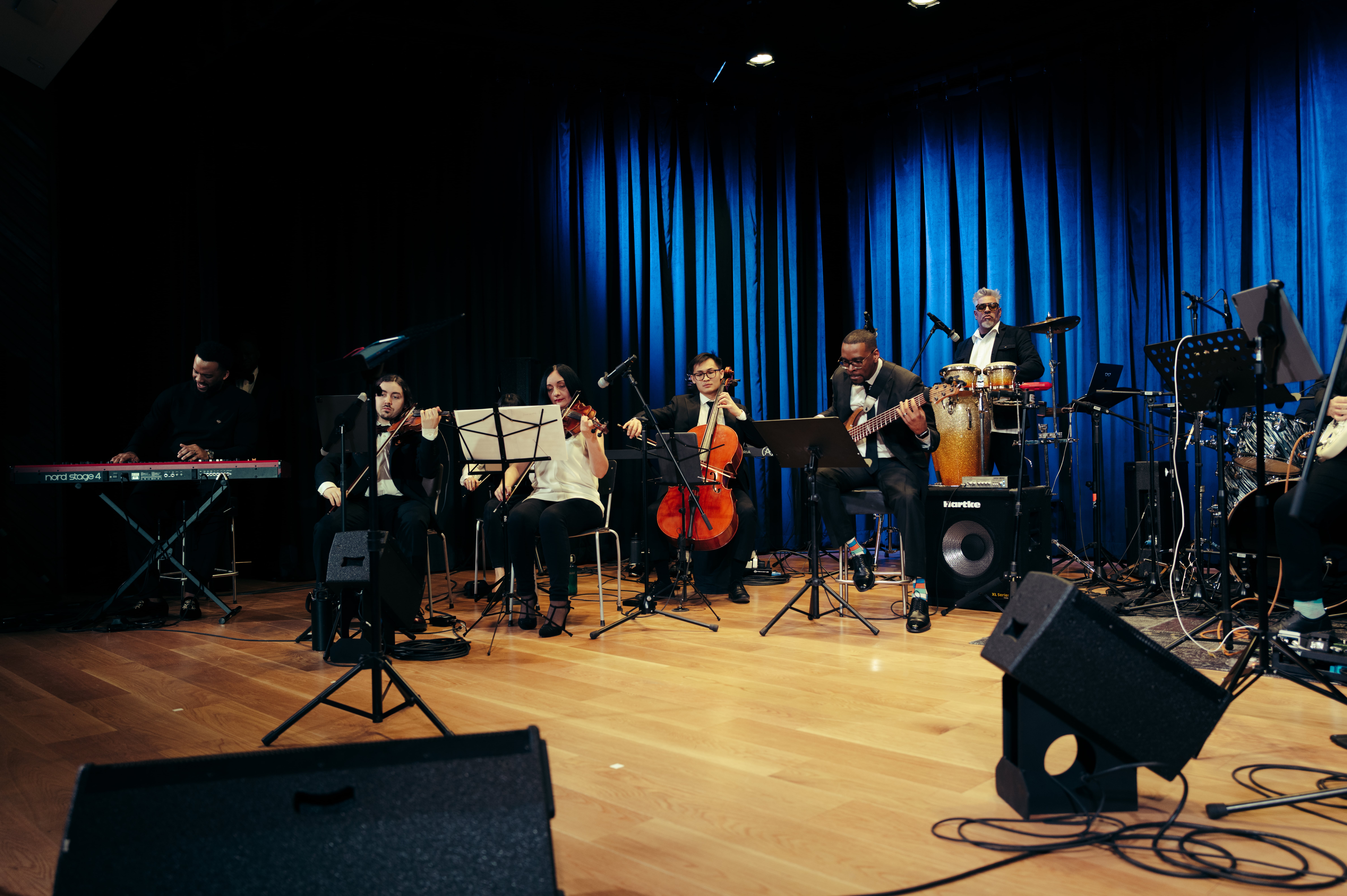 The Gbèdu Afro-jazz orchestral ensemble on stage with blue curtains